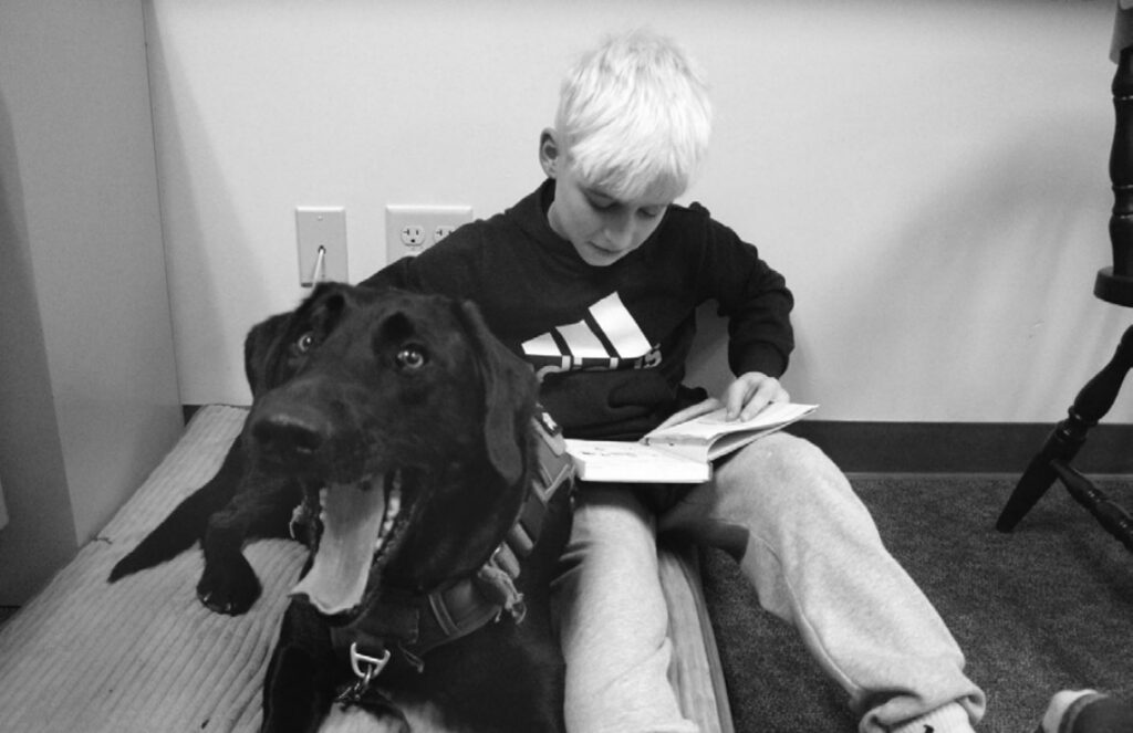 Pec middle schooler Bain Wiegel reads with Maverick, one of the district's two companion dogs, at his side. Wiegel says Maverick's presence uplifts spirits and builds confidence in him and his fellow classmates
