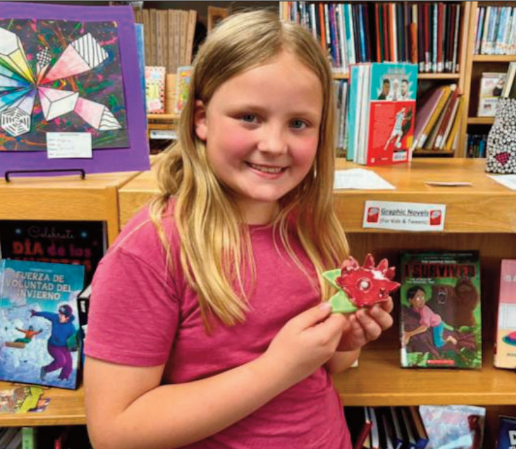 Clara, Grade 2, created a ceramic piece titled Monet's Lily. After learning about the French artist Claude Monet and his famous paintings of flowers, Clara was inspired to create her own interpretation of a water lily. She began by carefully shaping clay into forms that resembled a flower. Once the piece was formed, she applied glaze and had it placed in the kiln for firing. Clara shared that she was happily surprised by the colors after the firing process. To finish her artwork, she added a gem at the center of the lily, giving it a touch of sparkle.